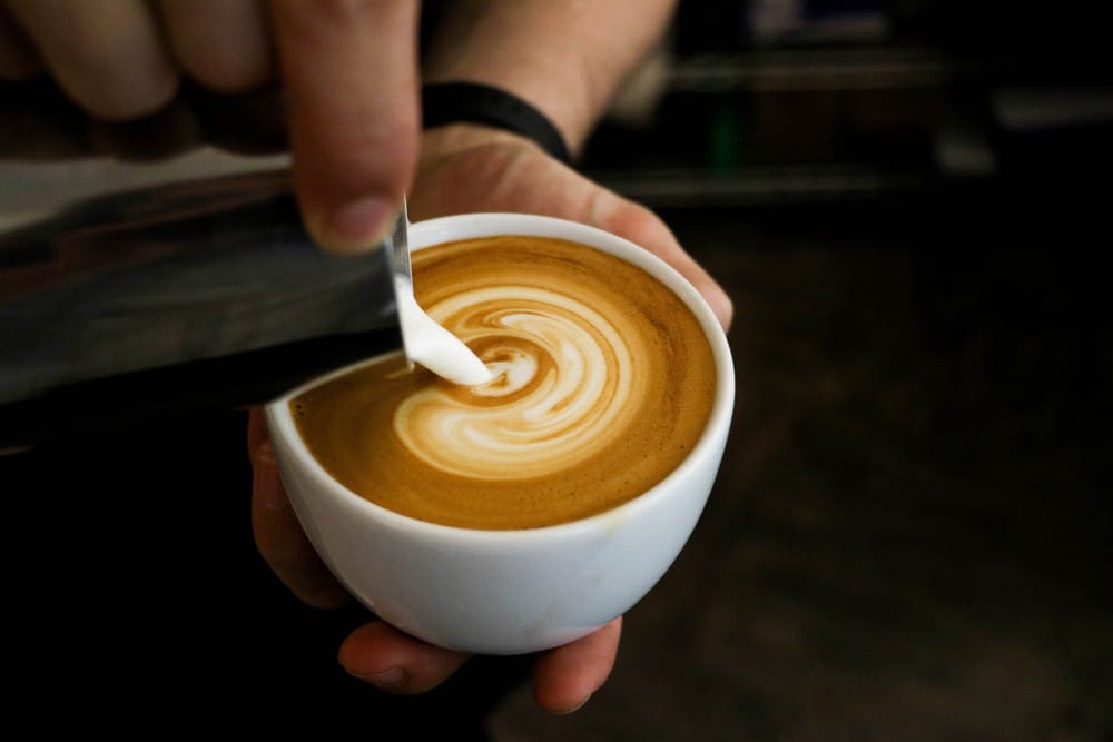 Vivir en Australia persona poniendo leche en un café